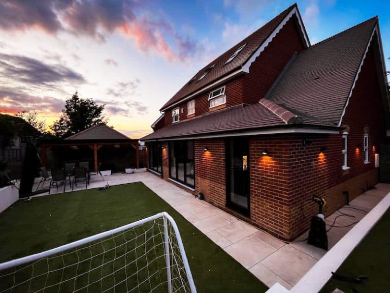 a finished house extension at dusk. the garden has a lawn with a football goal in the foreground. The house is face brick and has velux windows in the loft